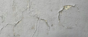 A close-up of a deteriorating plaster wall with cracks, chips, and exposed texture