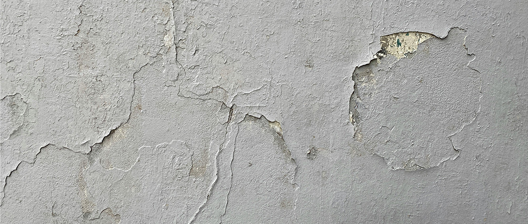 A close-up of a deteriorating plaster wall with cracks, chips, and exposed texture